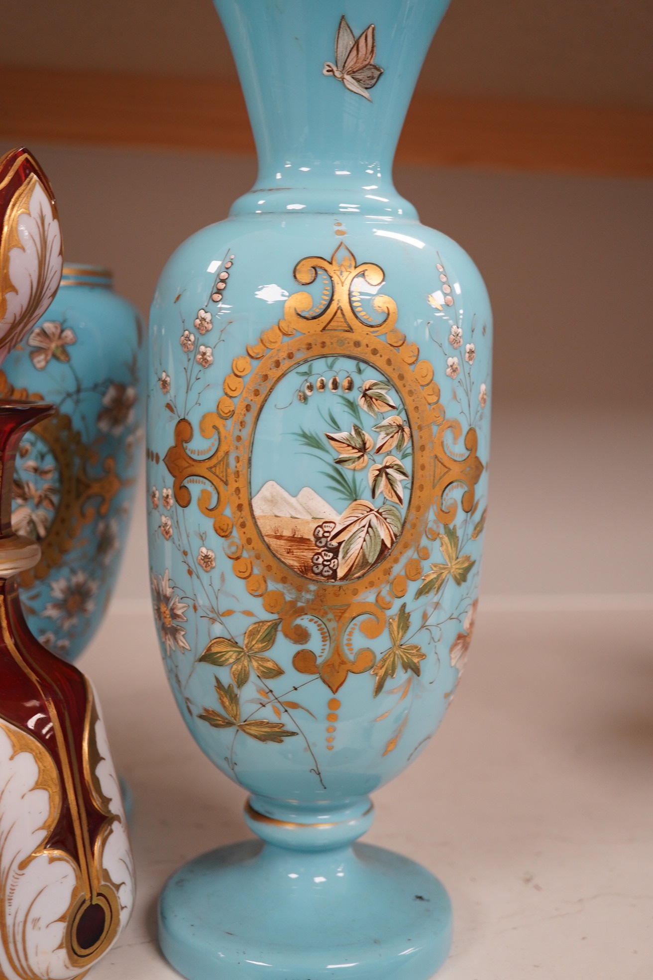 An enamelled glass garniture decorated with Egyptian scenes and a cranberry decanter, largest 29cm high. Condition - poor to fair